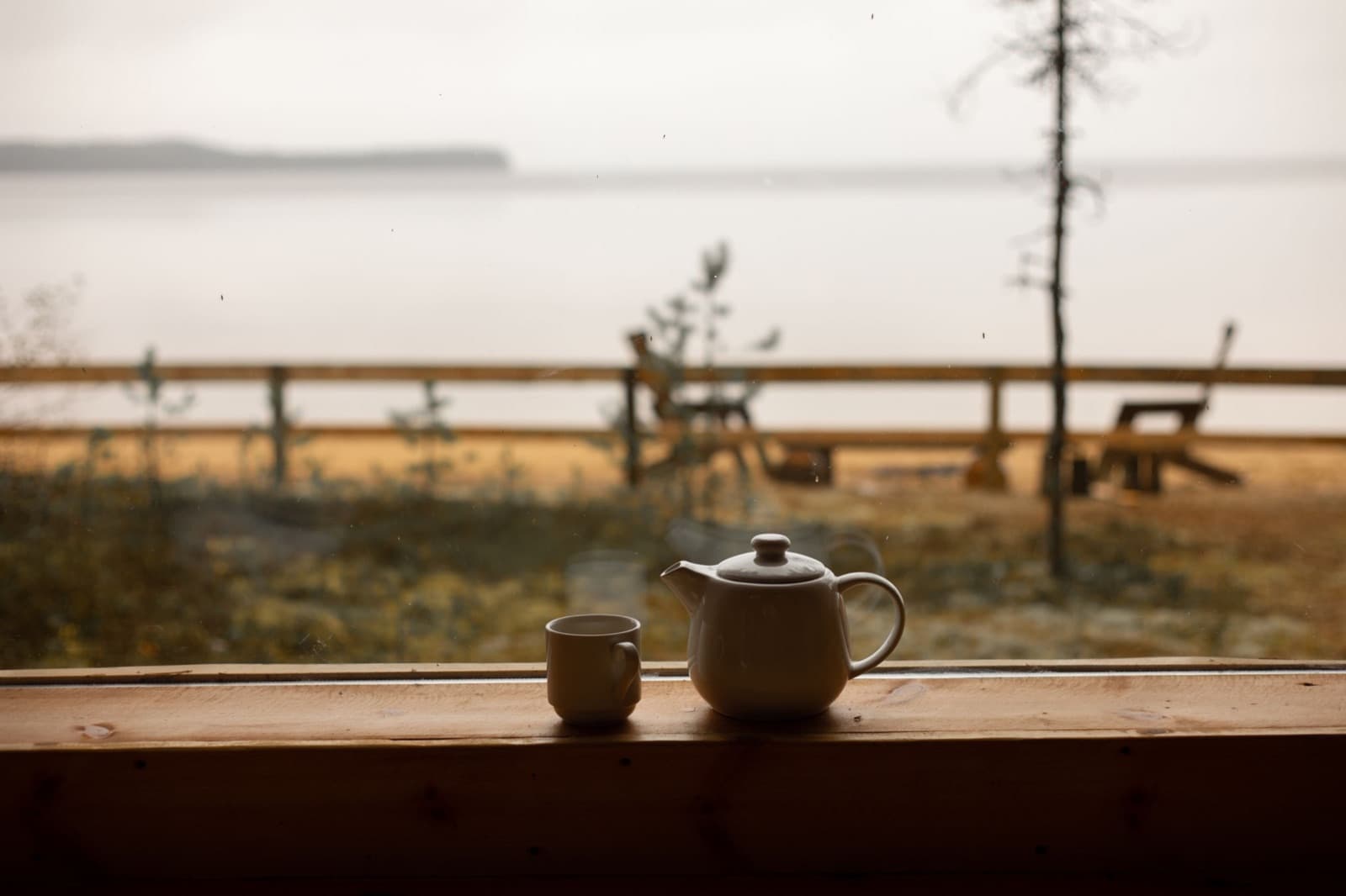 White teapot and cup on a wooden windowsill looking out over a misty lake in autumn